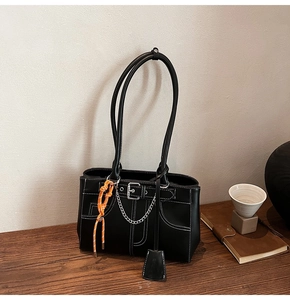 Dettaglio della borsa tote nera con cuciture bianche, catene metalliche e nappa arancione