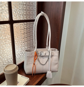 Chic cream white leather tote bag featuring chain details on a wooden window sill