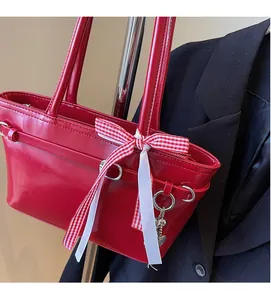 Détail du sac à bandoulière en cuir rouge brillant avec nœud à carreaux et breloque