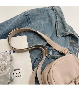 Detail of adjustable fabric shoulder strap on a beige nylon crossbody bag