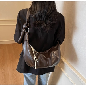 Detail of dark brown hobo bag with knotted strap and woven tassel on female model