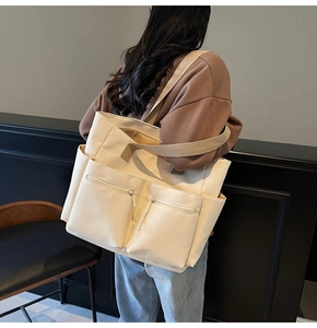 Detail of canvas tote bag showing large front pockets and wide woven shoulder strap on model