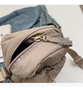 Detail of a khaki nylon crossbody bag featuring a smooth zipper with an extended puller