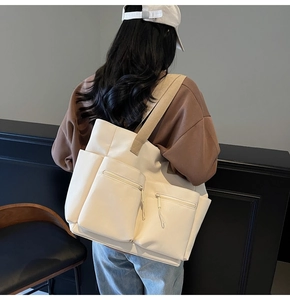 Detail of a large cream canvas tote bag with brown straps and utility zip pockets