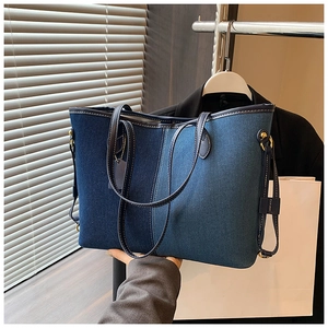 Détail d'un sac cabas en denim contrasté avec anses en cuir porté par un mannequin