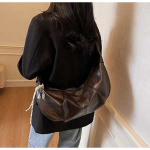 Detail view of large dark brown dumpling bag with pleated texture on female model