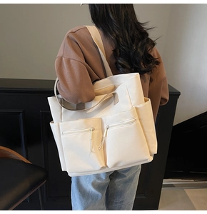 Detail view of cream tote bag with dual front zipper pockets and side pockets on shoulder
