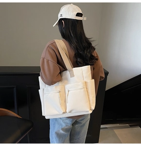 Detail of off-white canvas tote bag featuring double zippered front pockets and wide straps