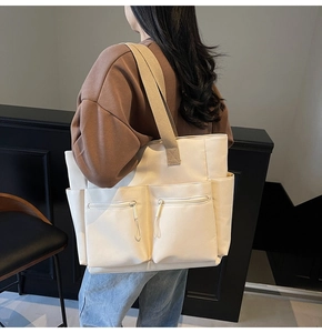 Model wearing a large beige nylon tote bag with multiple zip pockets for daily use