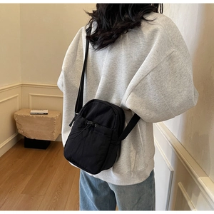 Rear view of a black drawstring crossbody bag worn over a casual sports outfit