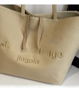 Detail of beige canvas tote bag with 3D letter embroidery and thick texture