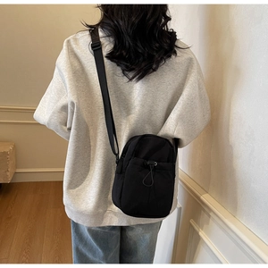 Rear view of a model wearing a compact black nylon crossbody bag with drawstring pocket