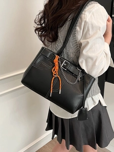 Black tote bag featuring denim pocket design, white stitching, and orange knot pendant