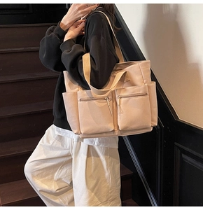 Detail of beige canvas tote bag showing front double zipper pockets and large capacity design