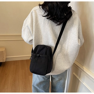 Detailed back view of a black drawstring crossbody phone bag worn over a grey sweatshirt