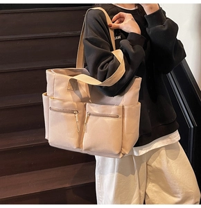 Detail of beige canvas tote bag with large front zipper pockets and wide shoulder straps