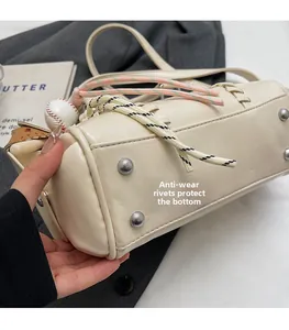 Detail view of wear-resistant rivets on the bottom of a cream cylinder shoulder bag