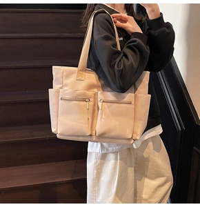 Detail of beige canvas tote bag showing dual front zipper pockets and side compartments
