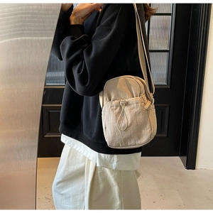 Detail of light beige nylon crossbody bag featuring drawstring pocket and zipper closure