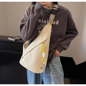 Detail of cream white sling bag featuring yellow carabiner and colorful lettered strap