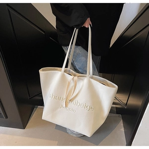 Close-up of cream canvas tote bag featuring embossed logo and durable slim handles