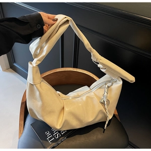 Detail of cream-colored pleated shoulder bag with knotted strap and heart charm decor