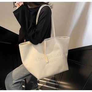 Detail of minimalist cream tote bag showing embossed lettering and long shoulder straps