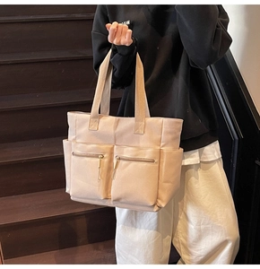Detail of beige canvas tote bag showing two front zipper pockets and side compartments