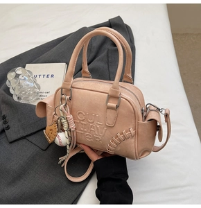 Detail of light pink Boston bag with embossed letters and baseball charm accessories
