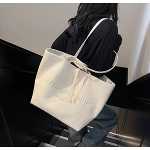 Detail of a large off-white canvas tote bag with embossed text on a female model