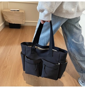 Detail of black canvas tote bag showing multi-pocket structure and wide handles