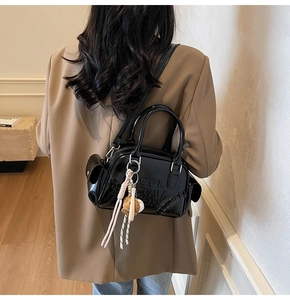 Detail of glossy black patent leather Boston bag featuring side drawstring and ball charm