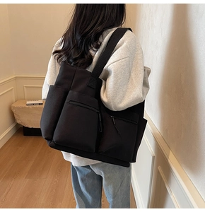 Close-up of black canvas tote bag with multiple functional pockets worn by a model