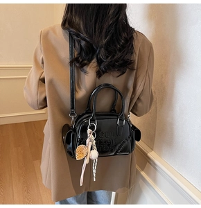 Detail of black glossy shoulder bag with embossed letters and a baseball pendant