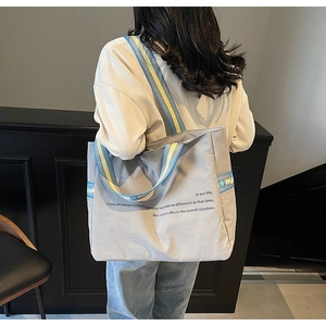Détail du sac cabas gris en toile avec bandoulière large à rayures bleu et jaune