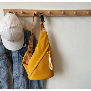 Detail of yellow canvas crossbody chest bag featuring bold branded strap and nylon zipper