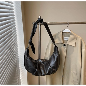 Detail of black leather hobo bag with knotted strap hanging near a beige trench coat