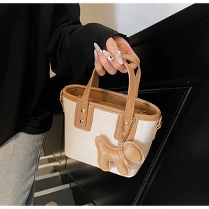 Detail der weiß-braunen Mini-Tote-Bag mit Sternprägung und süßem Hundeanhänger-Zubehör
