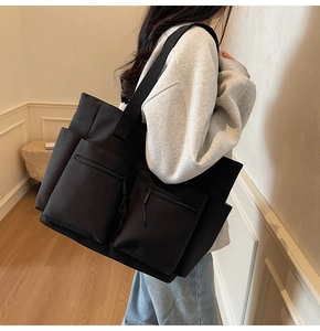 Detail of a black multi-pocket canvas tote bag showing zipper pockets and woven straps