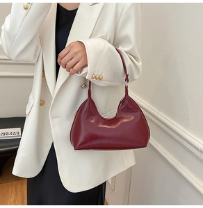 Detail of dark red glossy shoulder bag held by a model in professional white suit attire