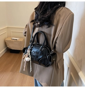 Detail of black glossy PU pillow bag with embossed lettering and stylish bag charms