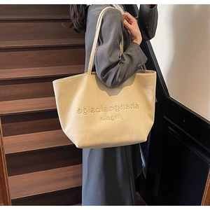 Detail of beige tote bag with litchi grain texture and embossed letters on shoulder