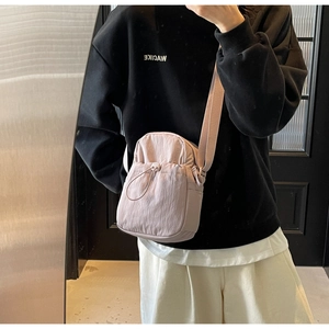 Detailed view of pale pink nylon crossbody bag with drawstring front pocket and wide strap