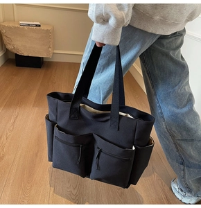 Detail of black canvas tote bag showing multiple functional pockets and wide straps