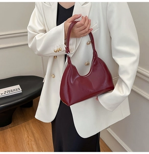 Close-up of a burgundy patent leather hobo bag with silver zipper on a white blazer
