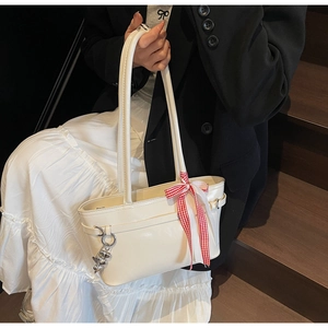 Détail du cabas en cuir verni crème avec ruban à carreaux rouges et pendentif