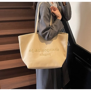 Detail of a beige tote bag showing high-quality leather texture and embossed lettering