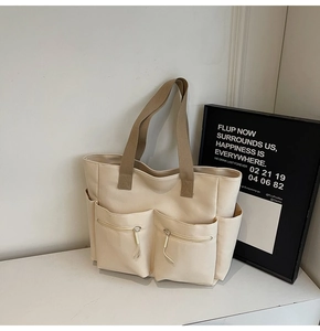 Detail of off-white canvas tote bag with front zipper pockets and brown handles
