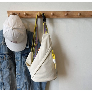 Detail of off-white canvas chest bag with vibrant yellow and purple branded strap