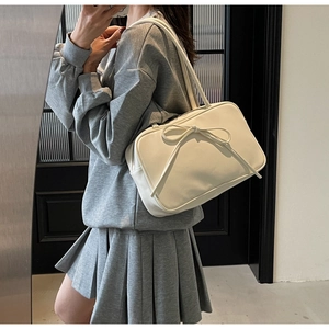 Detail of cream white shoulder bag featuring a stylish decorative bow and dual straps